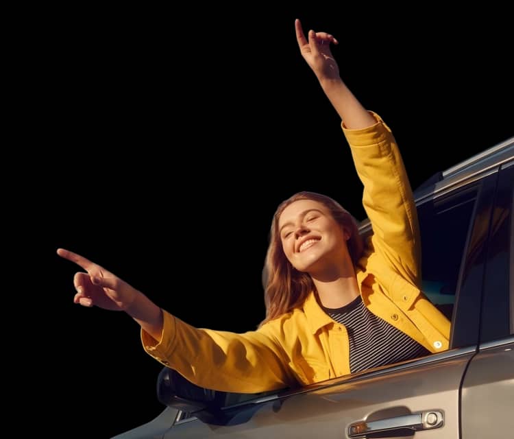 Moteris geltona striuke šypsosi iškišusi rankas pro automobilio langą